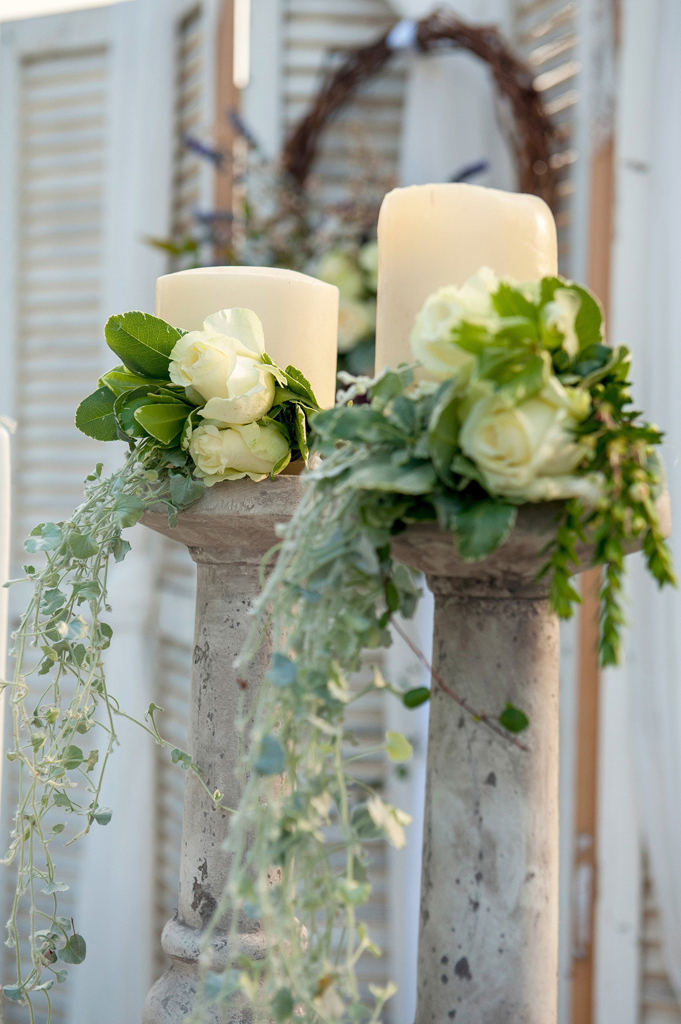 Διακοσμητικά κεριά με λευκά τριαντάφυλλα και πρασινάδες, σε ρομαντικό rustic στυλ.     Decorative candles adorned with white roses and greenery in a romantic rustic style.