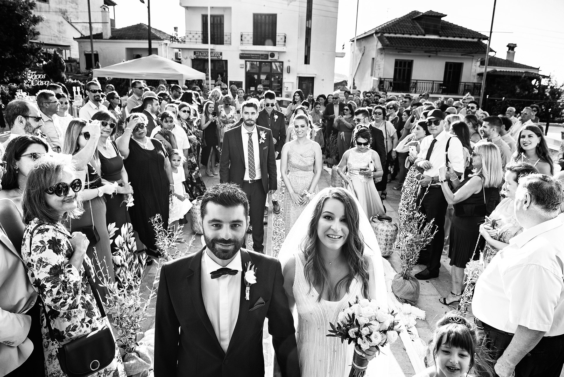 καλλιτεχνική φωτογραφία ζευγαριού μπροστά στην εκκλησία με τους φίλους τους πρίν ξεκινήσει η τελετή - φωτογράφος γάμου στη Χαλκιδική, artistic photo of a couple in front of the church with their friends before the ceremony begins - wedding photographer in chalkidiki