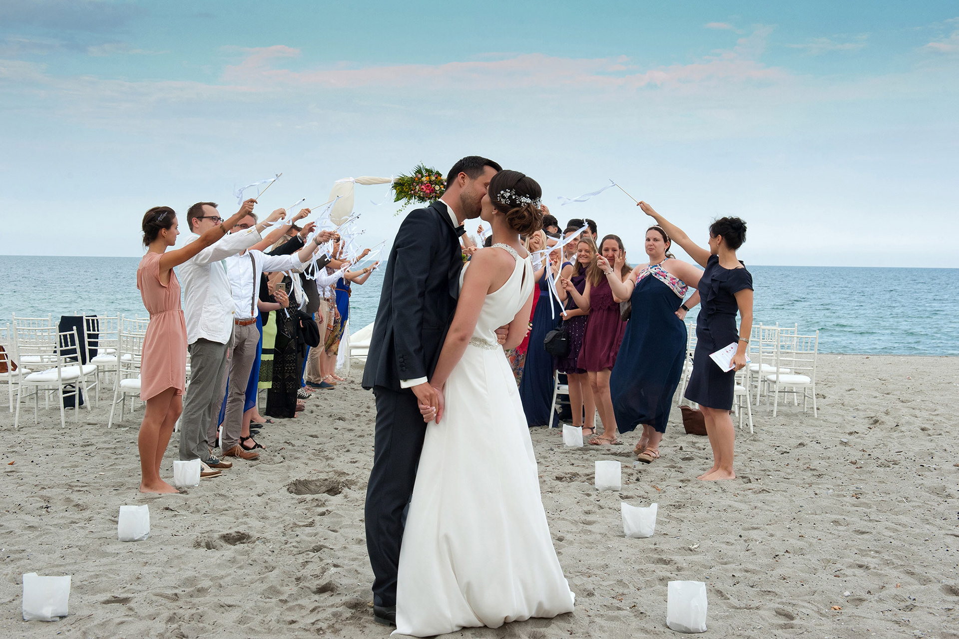 Οι νεόνυμφοι φιλιούνται στην έξοδο του γάμου ανάμεσα στους καλεσμένους. The newlyweds kiss at the wedding exit surrounded by guests.