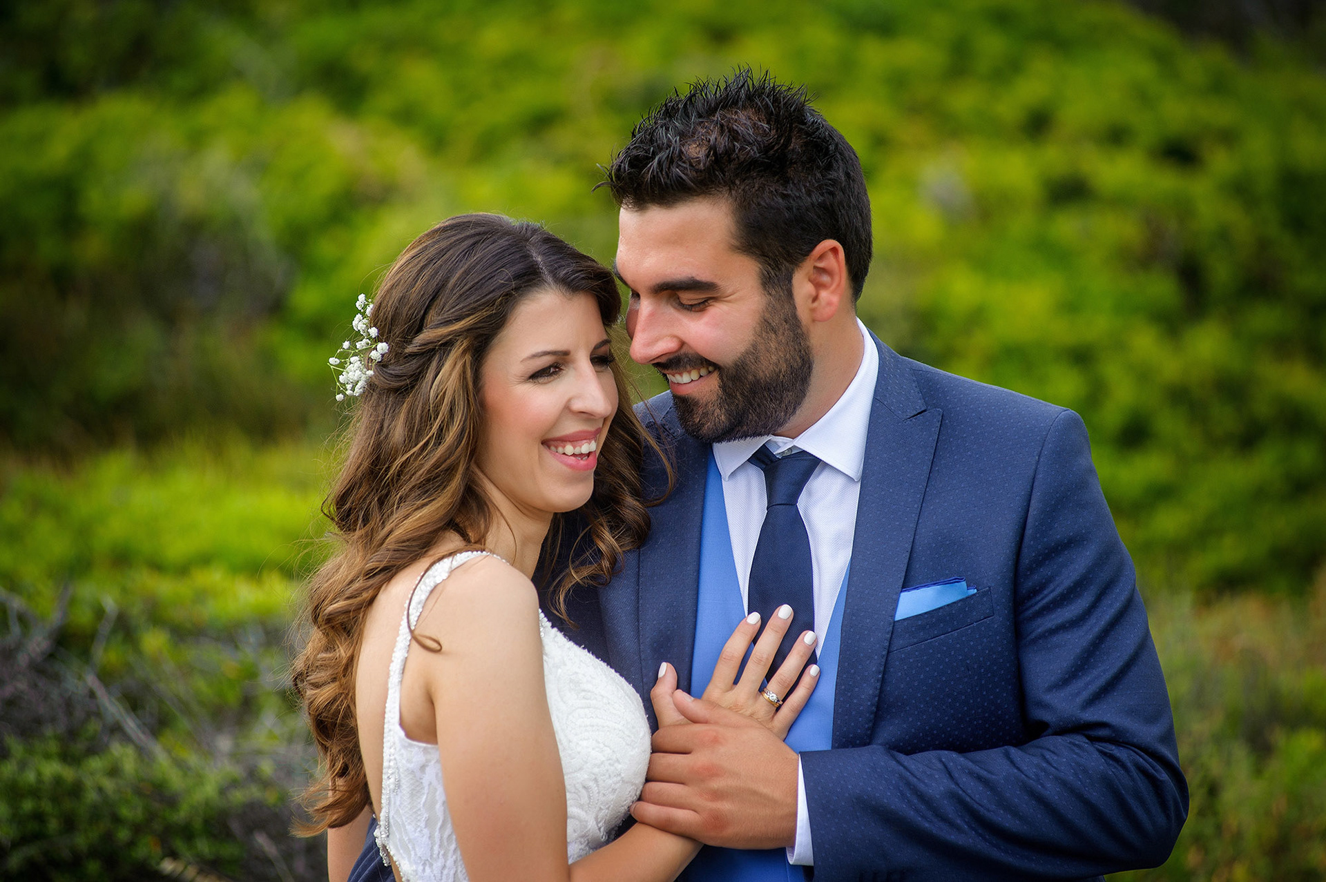 Ο γαμπρός και η νύφη γελούν ανέμελα στη φωτογράφιση μετά τον γάμο, με φόντο το πράσινο τοπίο της Χαλκιδικής.    The bride and groom laughing happily during their post-wedding photoshoot, surrounded by the green landscape of Halkidiki.