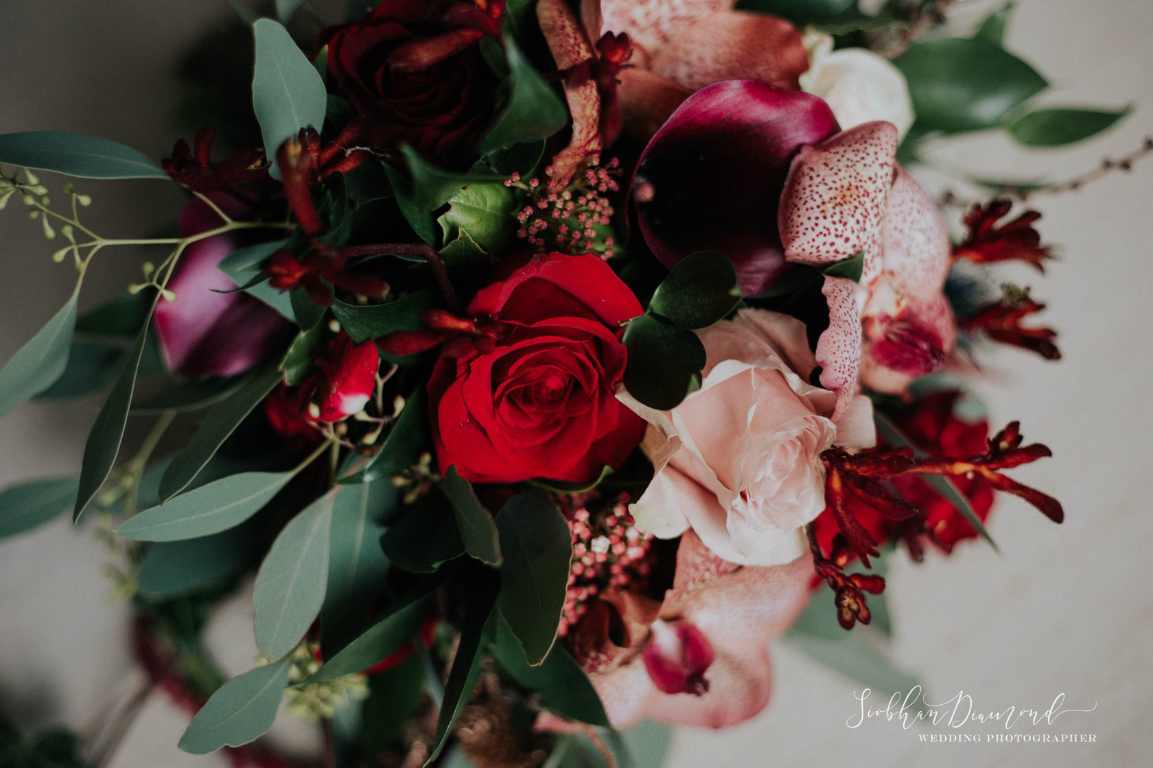 Brides bouquet of nude & red roses, golden orchids, calla lilies and foliage for a winter wedding