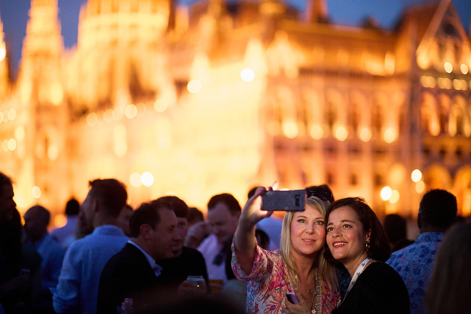 Conference participants capturing selfies with the Hungarian Parliament in the background.