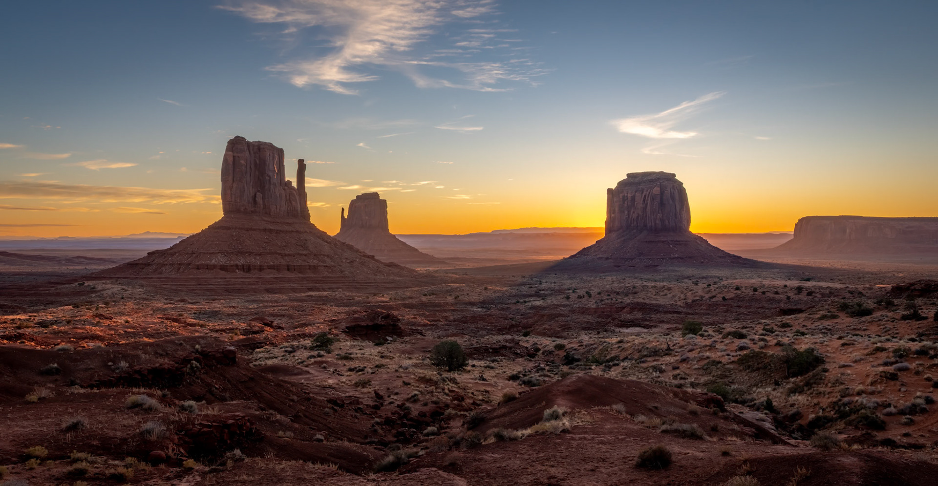 Monument Valley Sunrise - Sandstone mesas and buttes emerge as sunrise paints a warm glow across the valley.