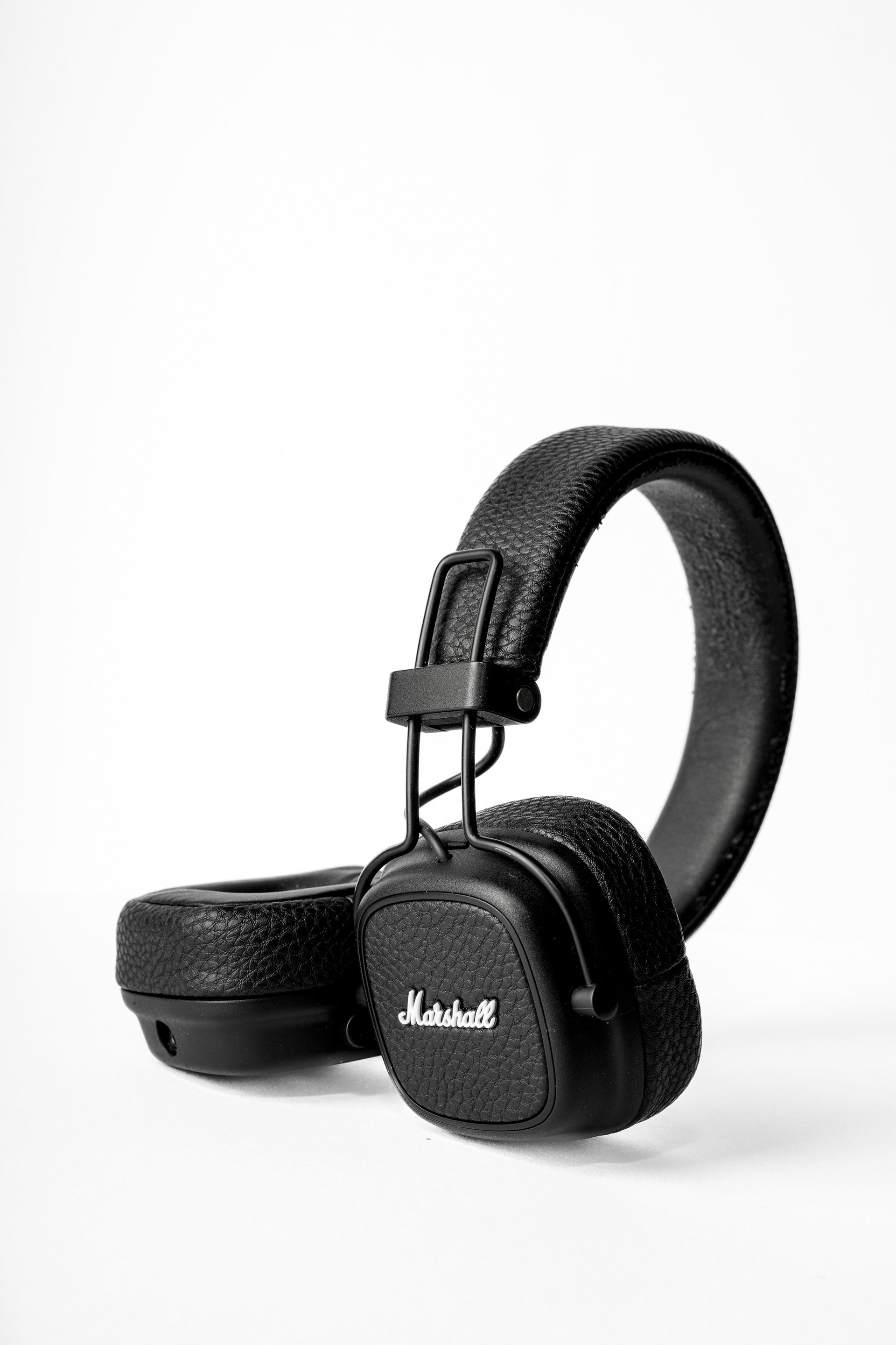 Produktová fotografie černých sluchátek Marshall s koženkovým povrchem na bílém studiovém pozadí. Minimalismus.