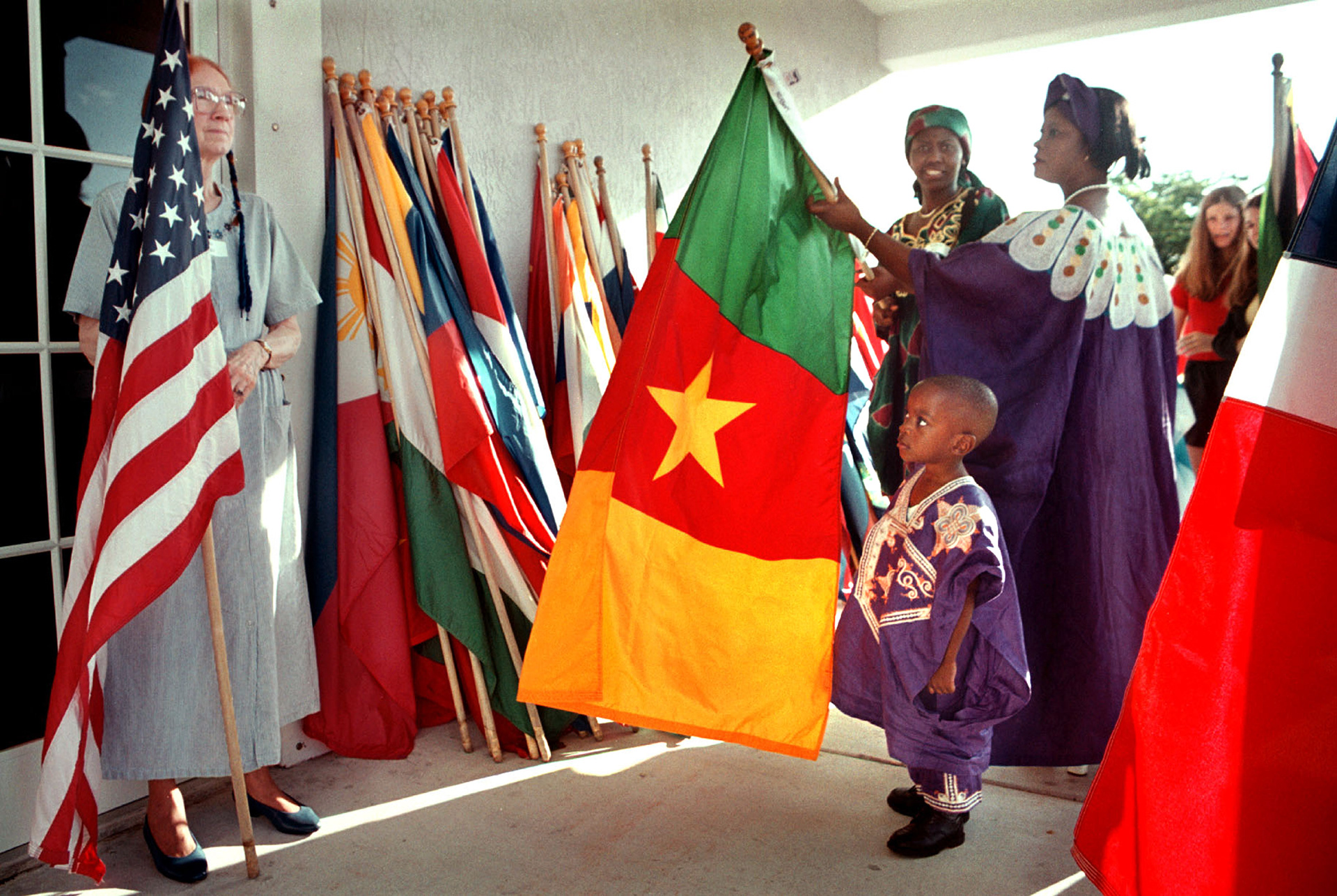 Bryant Muting, 3, peers past his native Cameroon flag to Veda Flynn and the American flag.