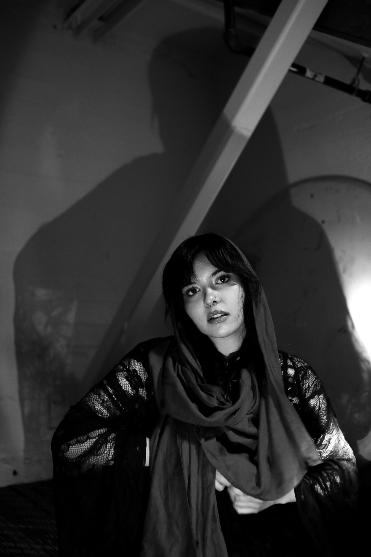 Sydney Spottiswood and her shadow appears above her, posing in a dormitory basement; February 14th, 2025.