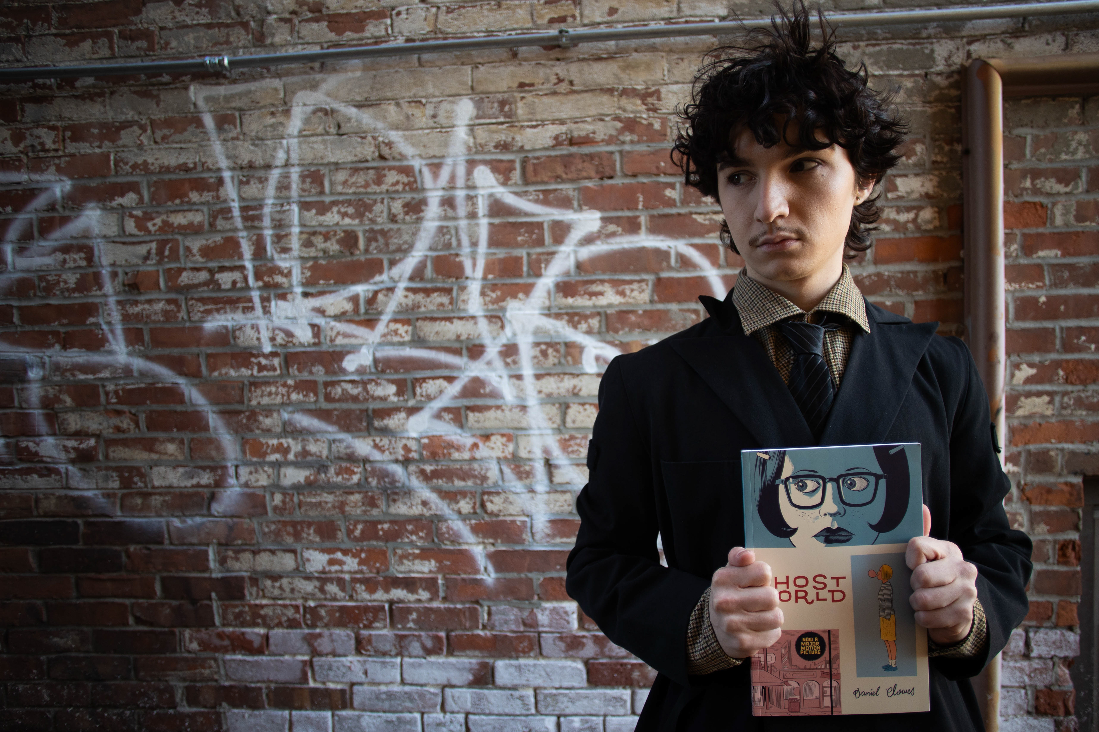 Ian Krockel holds their personal copy of Ghost World, a comic that they hold "near and dear to their heart," as they say while standing behind a graffitied wall; Febraury 28th, 2026.