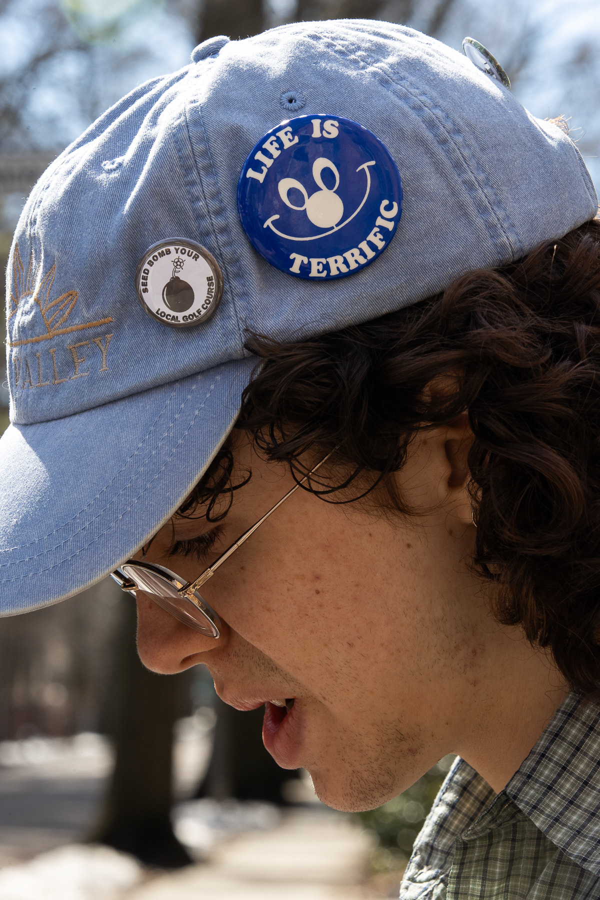 While Lucas Dantas Leite looks down toward their phone texting a friend, their bedazzled cap shows two vibrant and visually interesting buttons; March 9th, 2026.