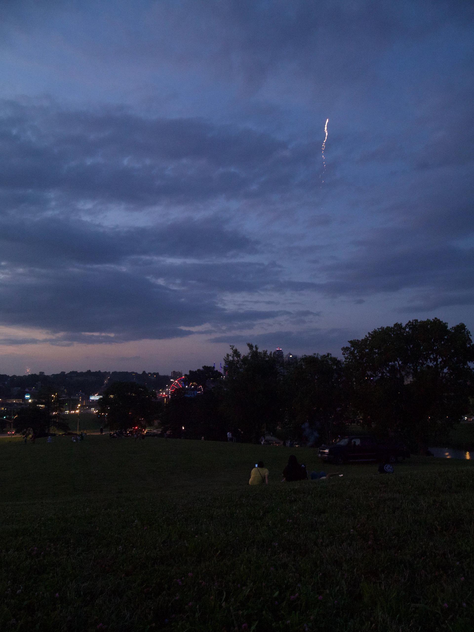 A family looks toward the sky as a firework launches into the sky before it explodes; July 4th, 2025.
