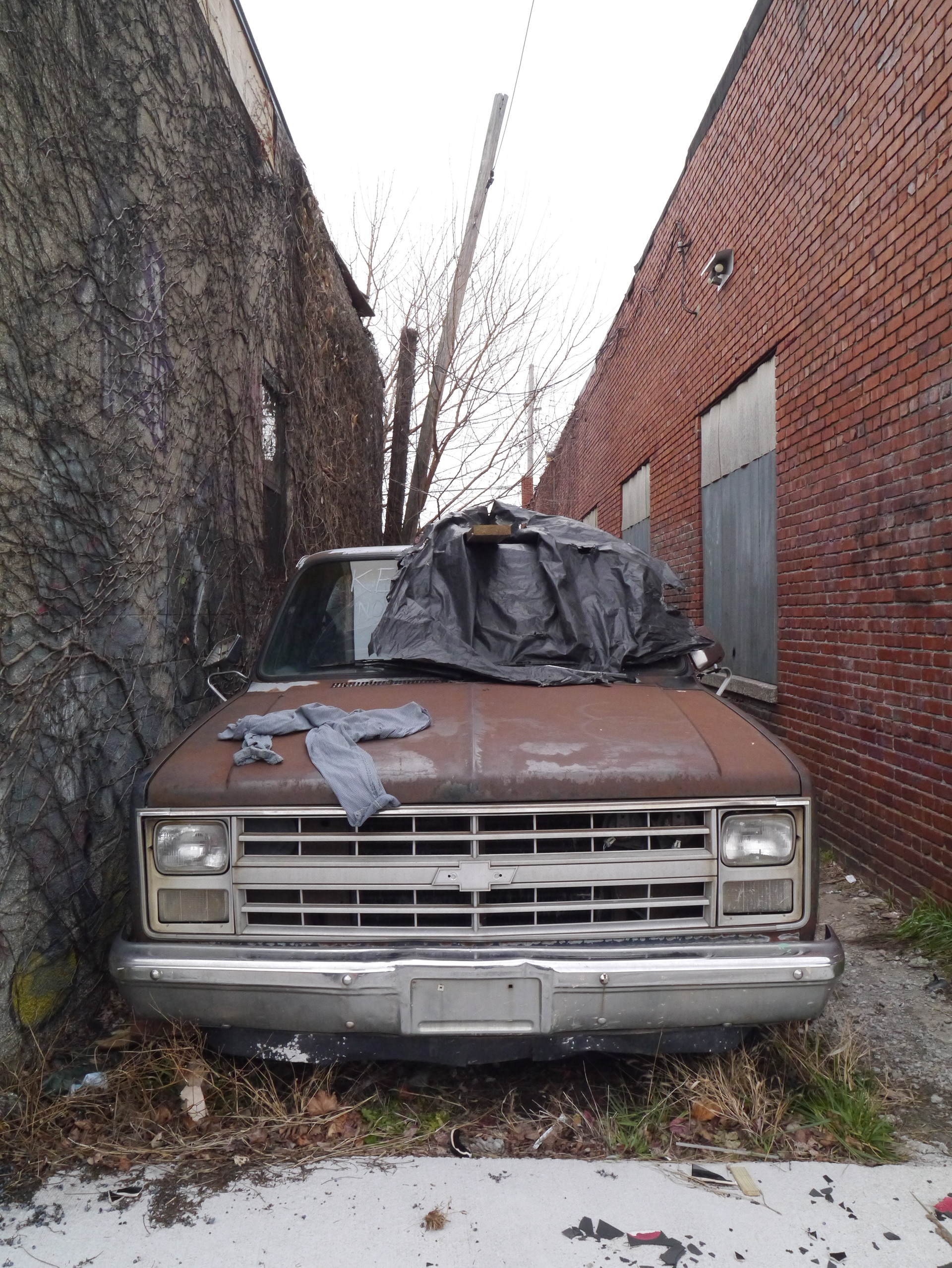 An abandoned, rusty truck that has piles of raggy clothing, sitting between two brick buildings on Locust Street in Kansas City, MO; December 31st, 2023.