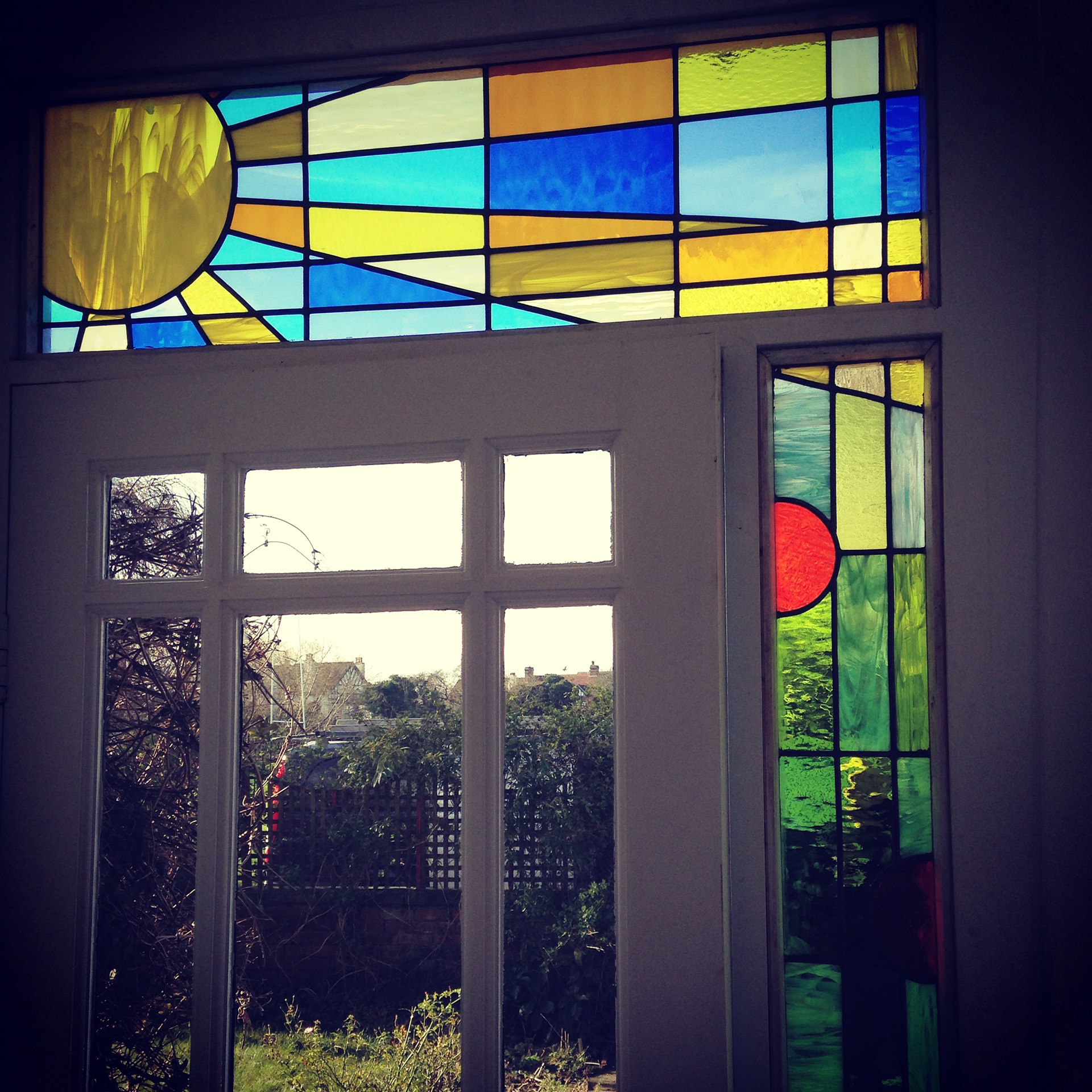 Stained glass in Headingley Leeds. Original Clarice Cliff themed design in art glass. Sunshine, sunbeams with abstract nasturtiums for external wooden door frame - seen from the inside with a heavy contrast filter