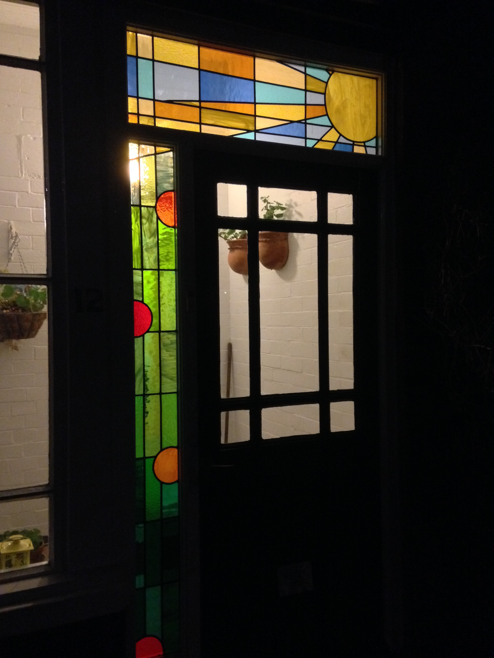 Stained glass in Headingley Leeds. Original Clarice Cliff themed design in art glass. Sunshine, sunbeams with abstract nasturtiums for external wooden door frame - seen from the outside at night