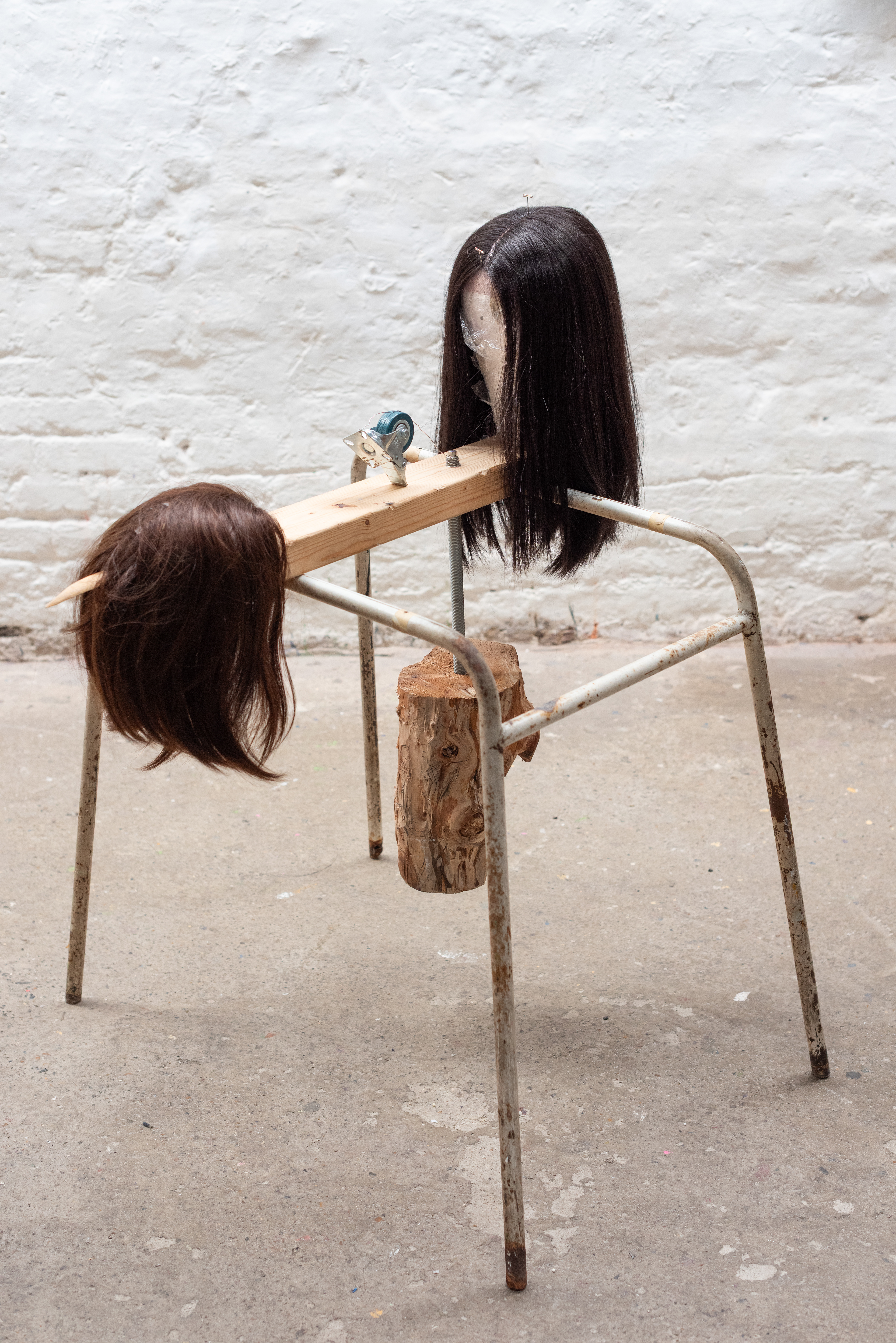 Tabby Li - Prey - (2024) -  Found object, human & synthetic hair, log, stainless steel wire, heavy duty swivel rubber wheel, T pins, wood, wig block, cling film & stainless steel threaded rod  - 107 x 92 x 75cm