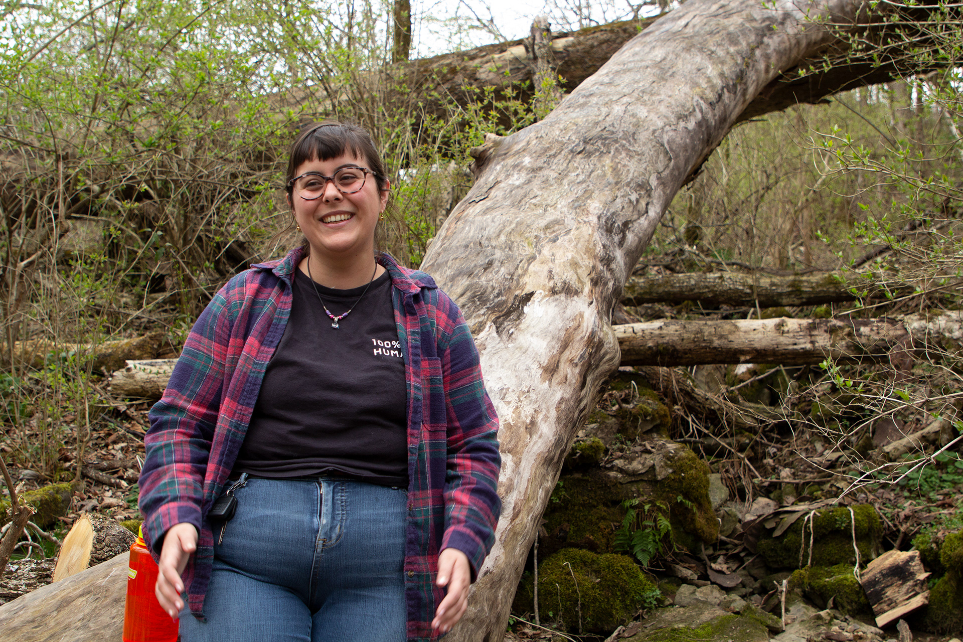 The artist is pictured smiling in front of a fallen tree beside a hiking trail. She has her water bottle and car keys clipped to her belt - very responsible!