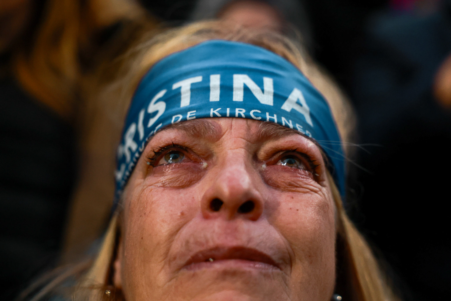 A woman looks on as Cristina Fernández de Kirchner greets supporters from the balcony of her home on her first day under house arrest following her conviction in the “Vialidad” corruption case | Buenos Aires, 2025.