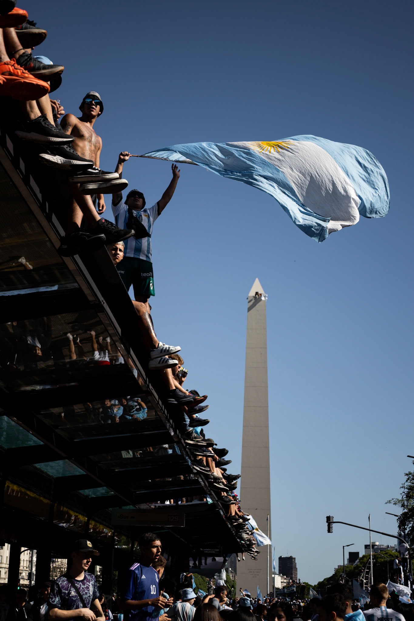 People stand on top of a bus stop shelter during celebrations for Argentina’s FIFA World Cup Qatar 2022 victory | Buenos Aires, 2022.