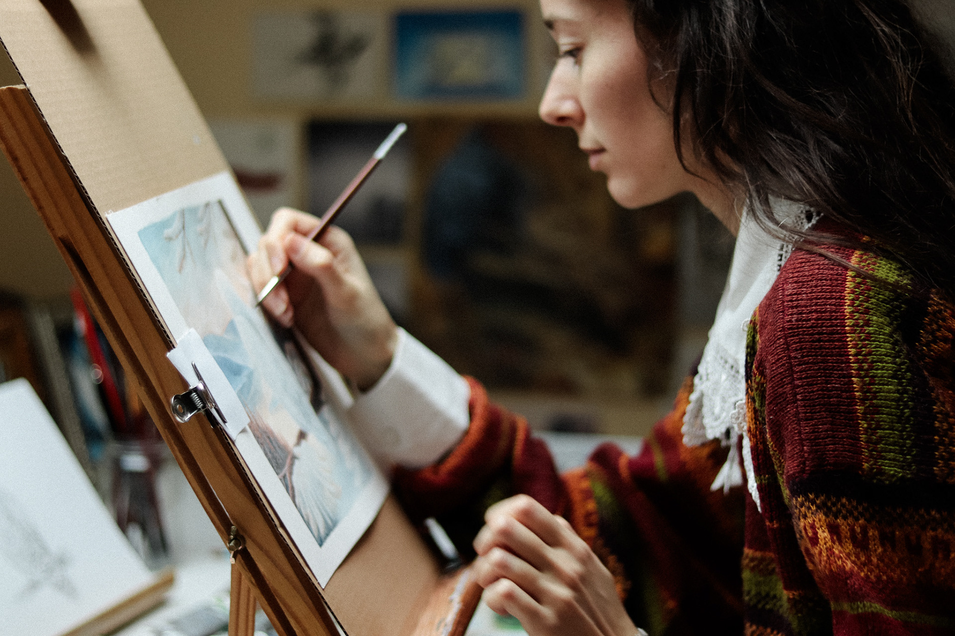 Portrait de Léa Mrdjenovic peignant dans son atelier sur chevalet. Artiste-peintre et illustratrice dans le Lot.