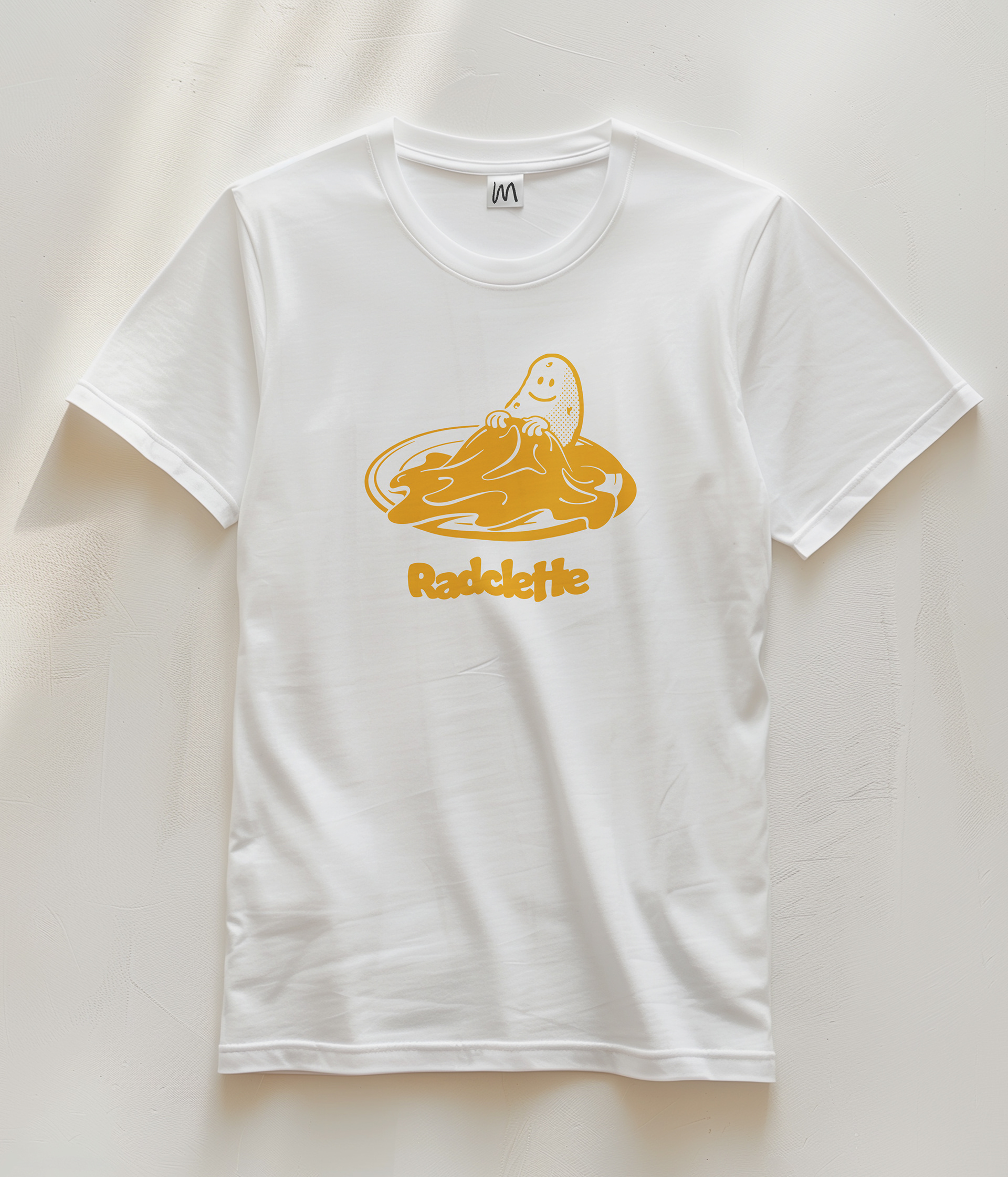 Ein Foto von einem weissen T-shirt auf dem eine Illustration von Maurus Zehnder zu sehen ist. Die Illustration zeigt wie sich eine Kartoffel mit Raclette zudeckt.