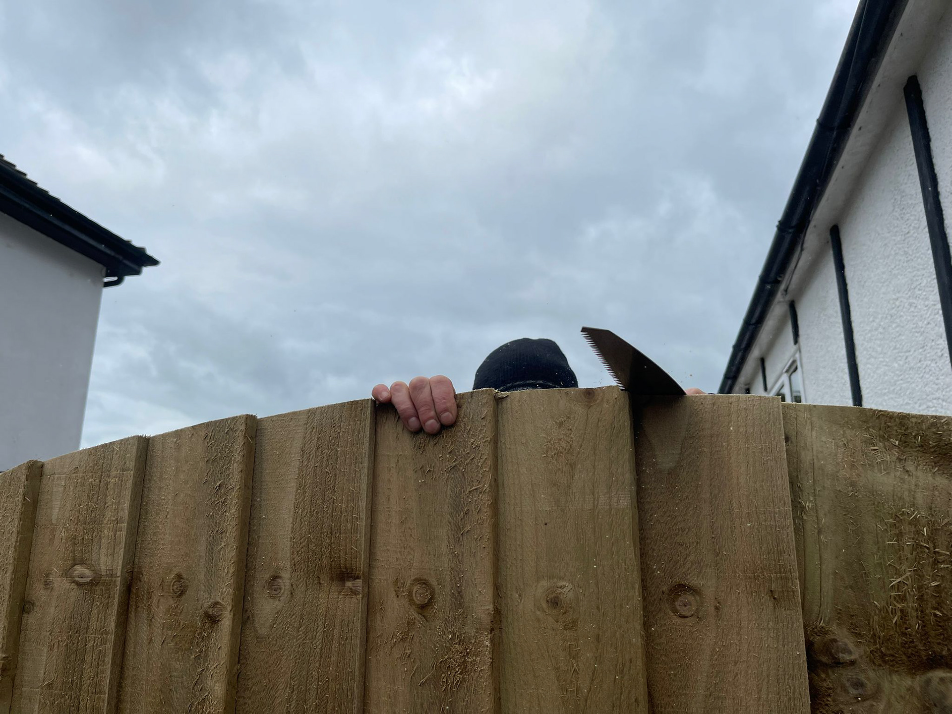 Workman sawing a curve on the top of a fence pannel