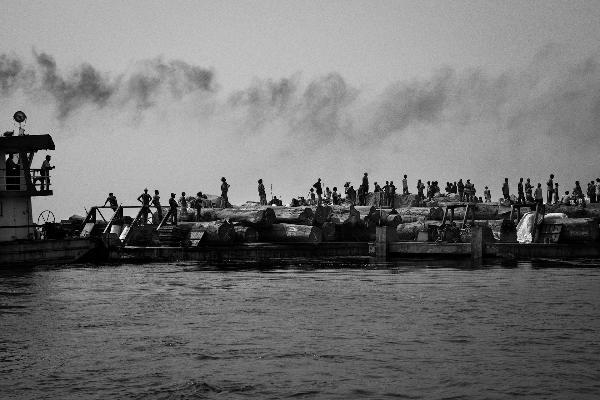 Kinkole, Kinshasa province, June 2016. A towboat with barges loaded with logs and passengers. Local populations often use these boats to travel and do business. The Congo river is the main way to transport wood produced in the DRC to the harbor of Kinkole, the biggest wood market of the country. Some logs travel up to 1,200km on the river, the only communication axis to cross the DRC.