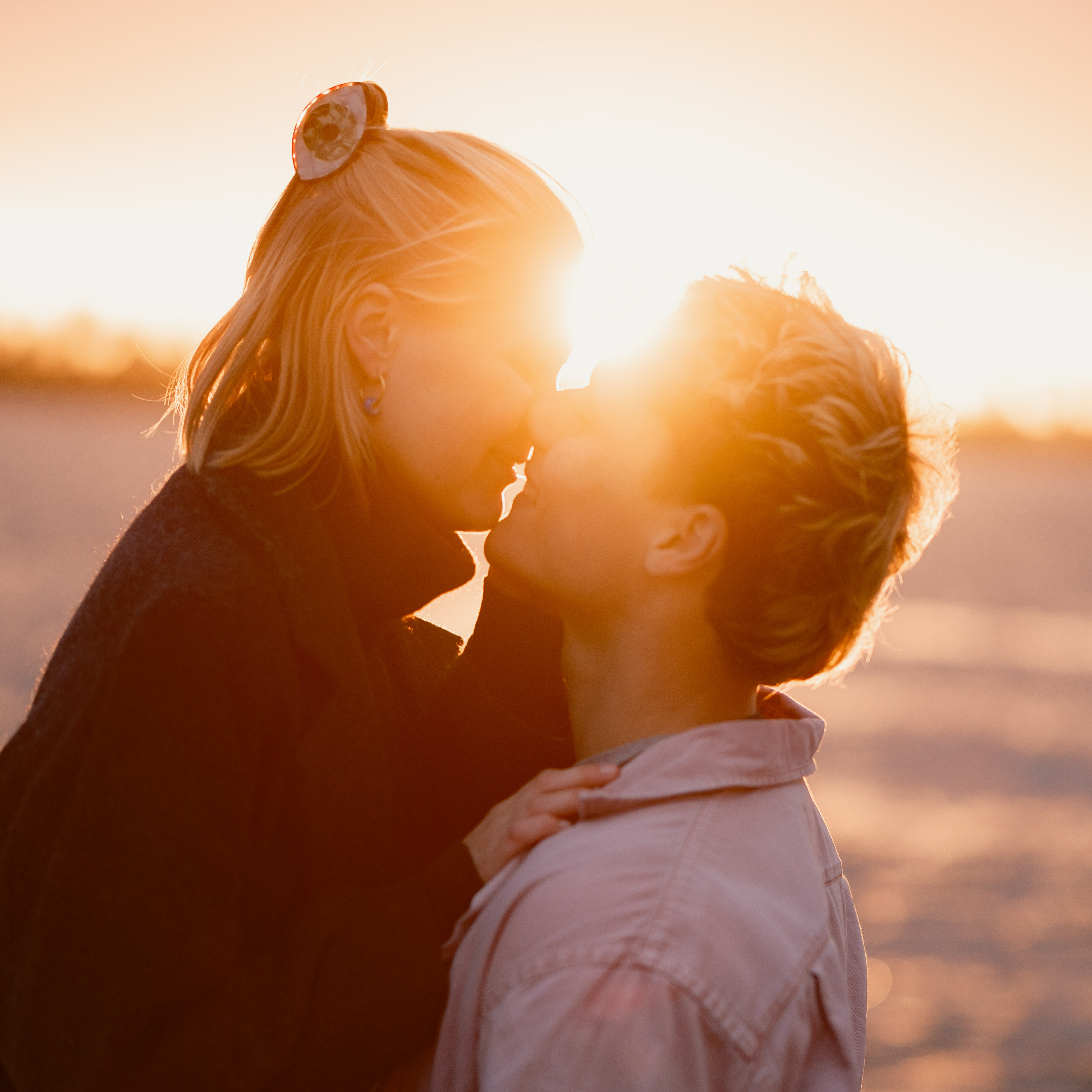 Verliebtes Paar küsst sich direkt vor der untergehenden Sonne des Elbstrands. Die Sonnenstrahlen strahlen über das ganze Bild. Es ist sehr warm und beide sind sehr glücklich.