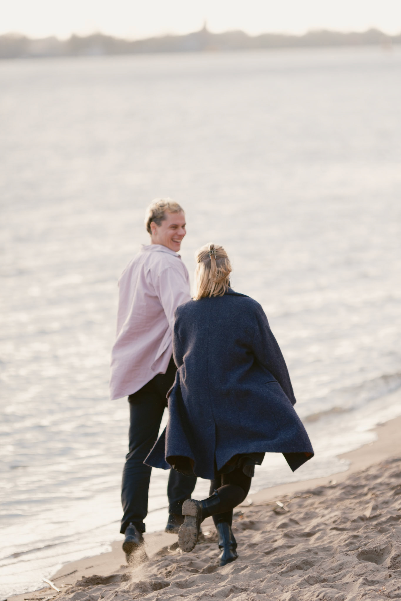Verliebtes Paar läuft am Elbstrand entlang. Er lächelt zu ihr zurück. Beide sind frisch verlobt und nutzen die entstandenen Bilder für ihre Einladungskarten. Das Bild hat eine künstlerische Unschärfe.