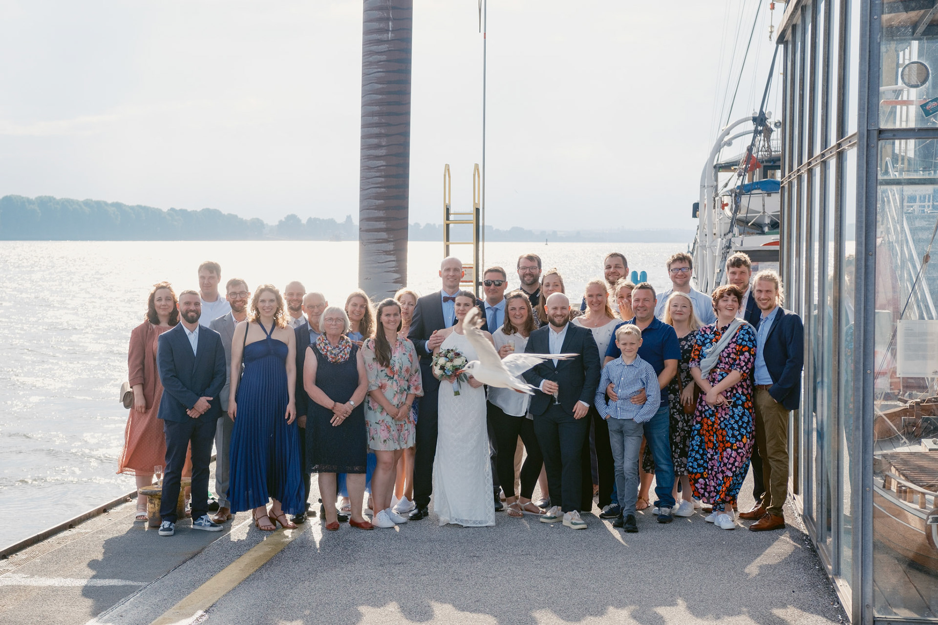 Gruppenfoto von einer Hochzeitsgesellschaft am Hamburger Hafen. Im Vordergrund sieht man eine Möwe die direkt durch das Bild fliegt.