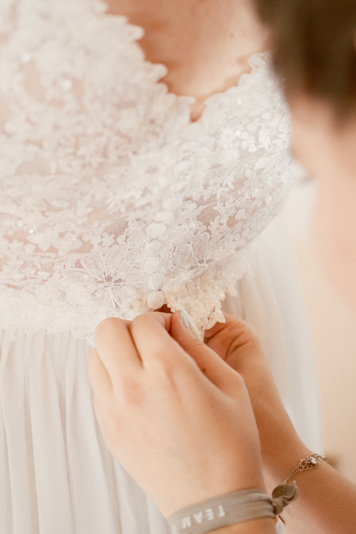 Der Braut wird ihr Brautkleid von der Trauzeugin zugeknöpft. Ein typisches Motiv bei einem Getting Ready am Anfang eines Hochzeitstages.