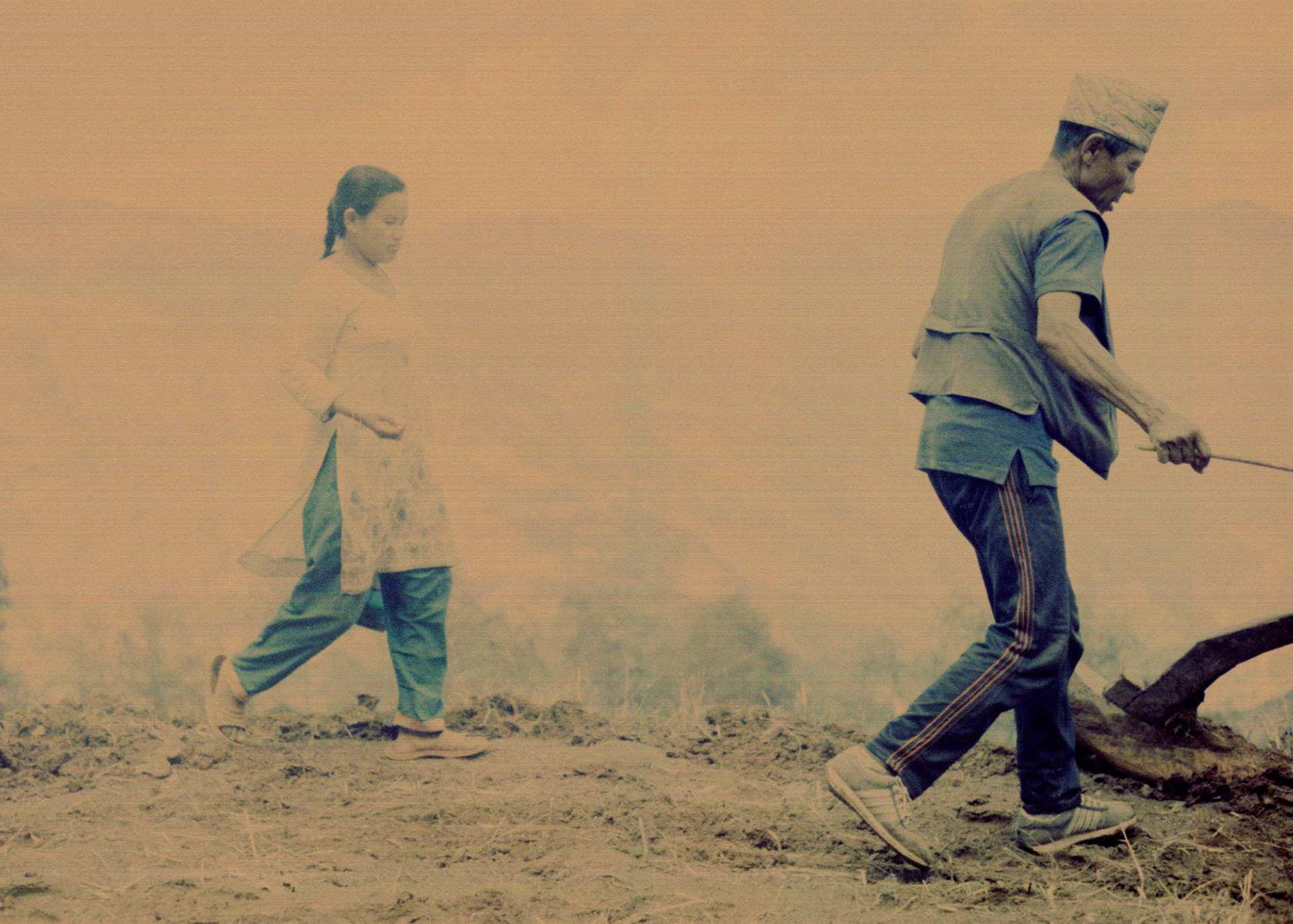 Jirel drops corn seeds into the soil while a man she has hired plows the soil with two oxen. 