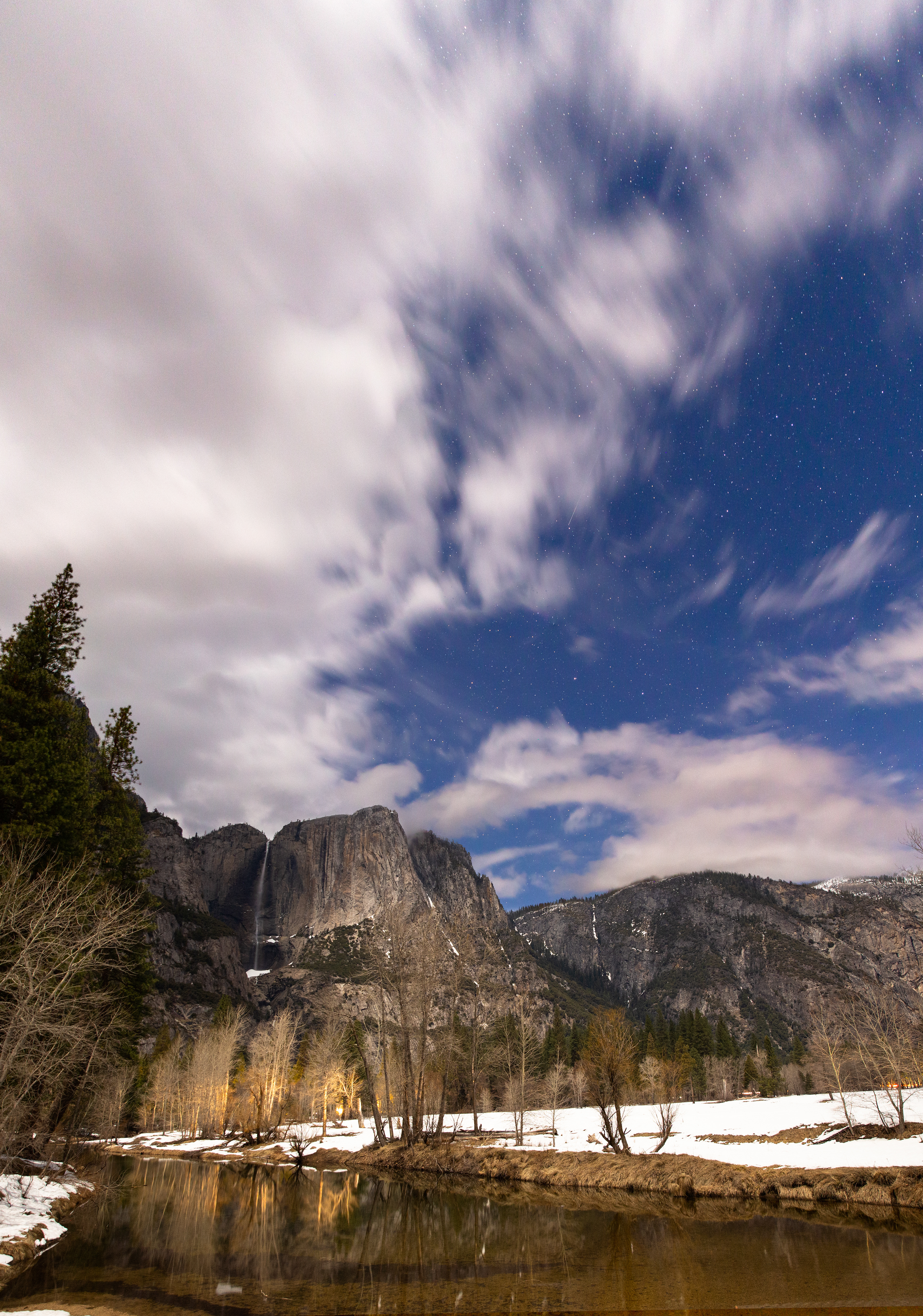 Yosemite Falls flows over the Merced River under moonlight in Yosemite NP.