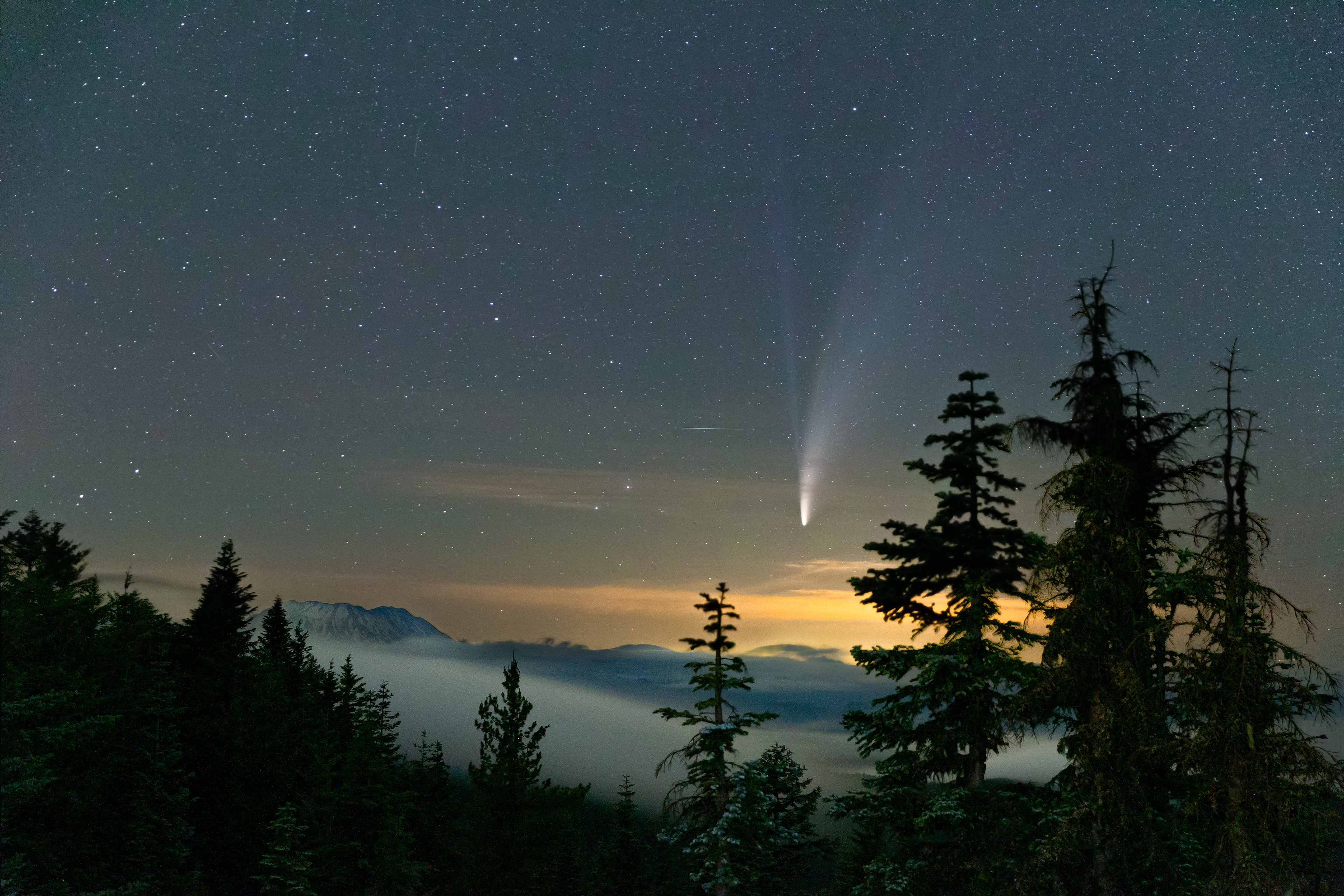 The comet NEOWISE glows in the sky next to a fog-covered Mount St. Helens from Obersation Peak, 