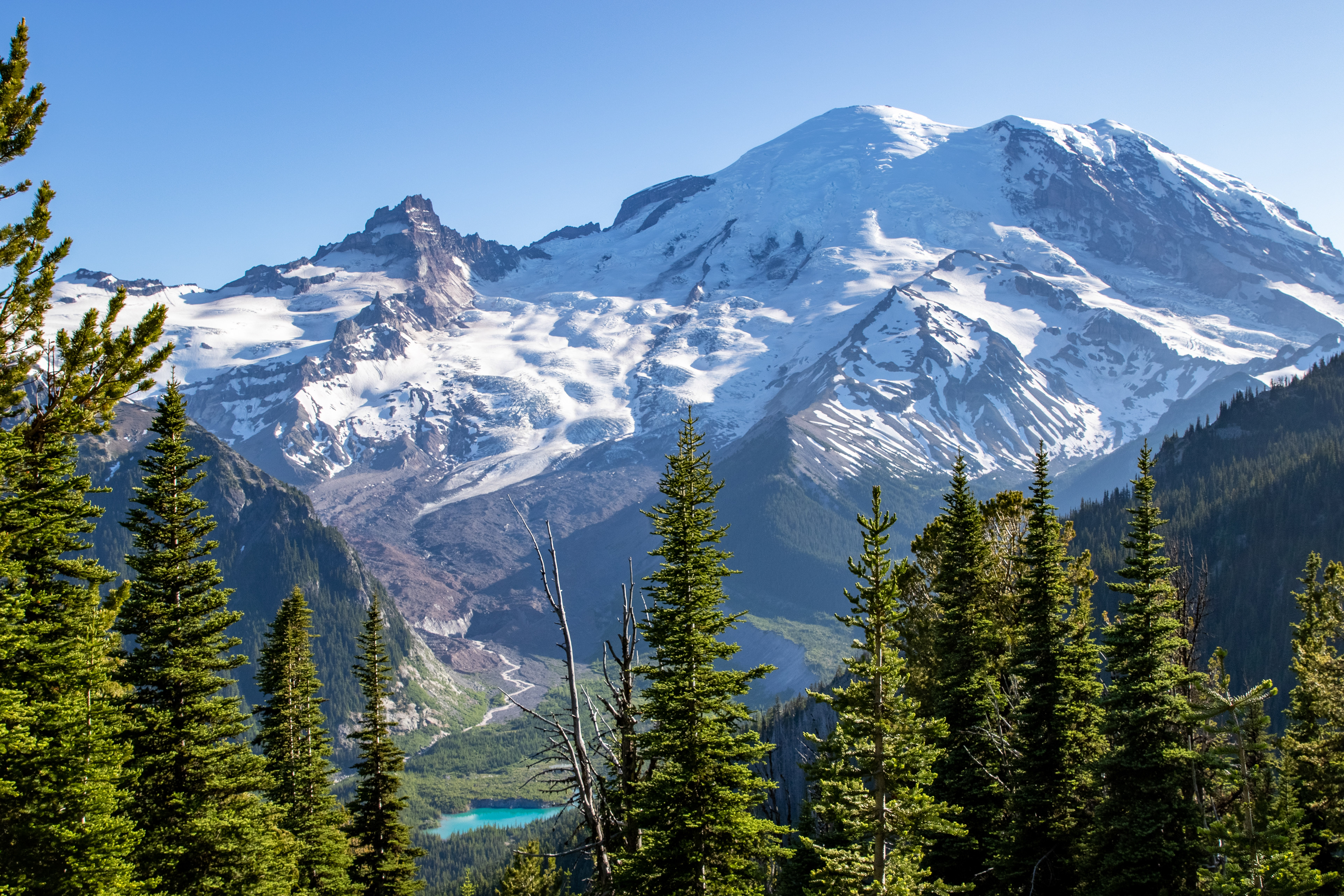 Mount Rainier stands tall over an emerald blue glacial lake at its base.