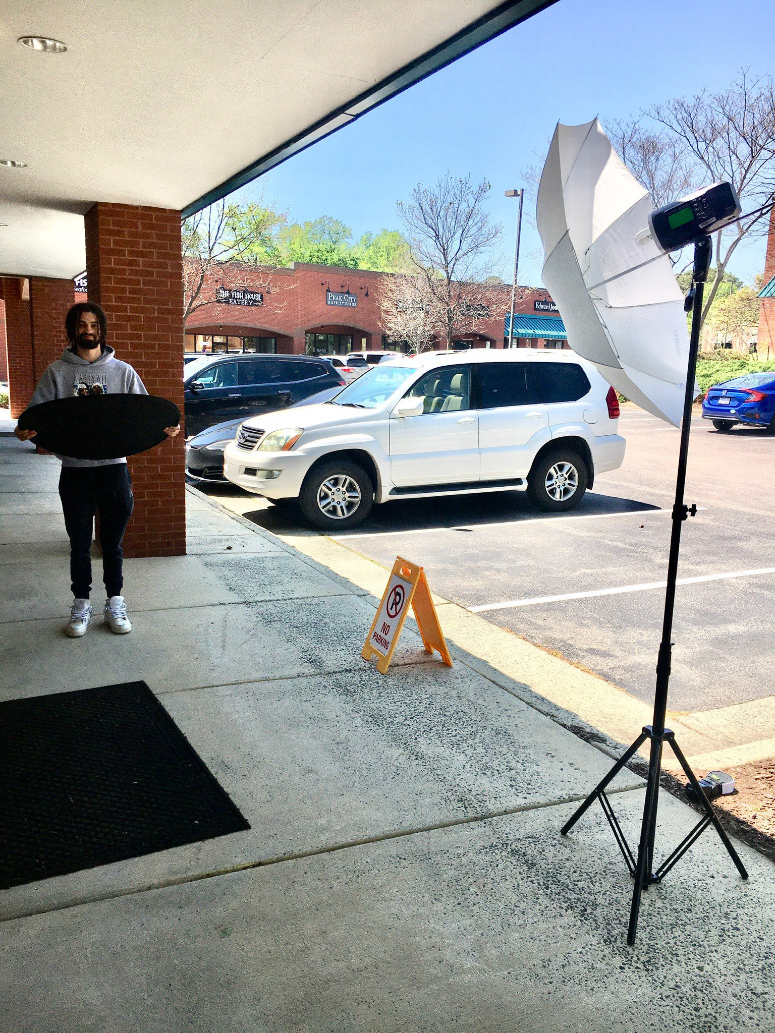 Employee Jalen holding my reflector while I use a strobe light under the shade to take his portrait.