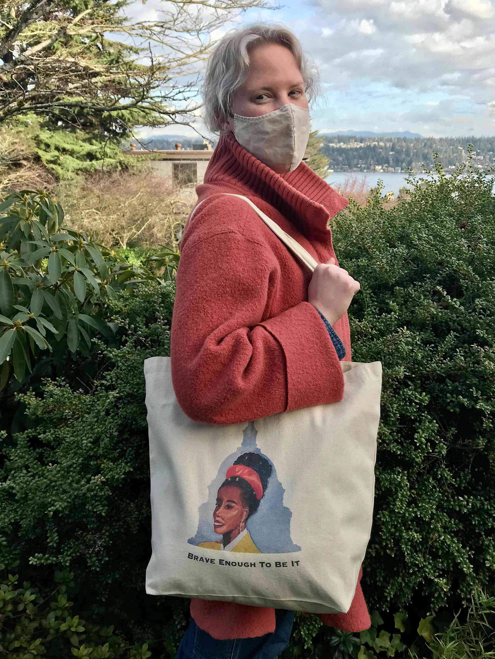 Woman holding a bag with a painting of Amanda Gorman on it. Lake in background.