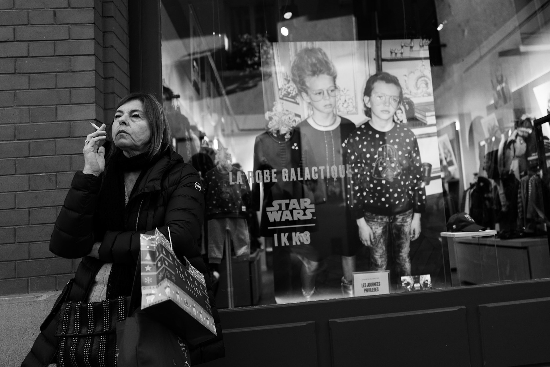 Femme fumant une cigarette devant la vitrine d’un magasin, à côté d’une affiche publicitaire Star Wars montrant deux enfants sérieux et lunettés.