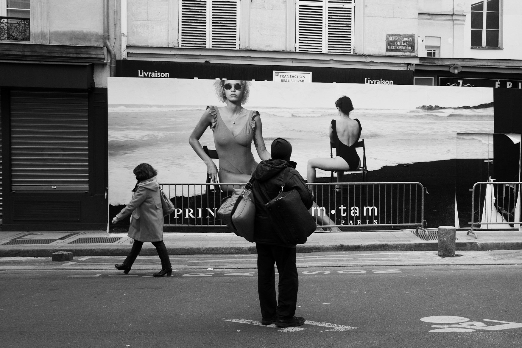 Un passant s’arrête devant une grande affiche de maillots de bain, semblant interagir avec les mannequins géants en arrière-plan, dans une mise en scène involontaire.