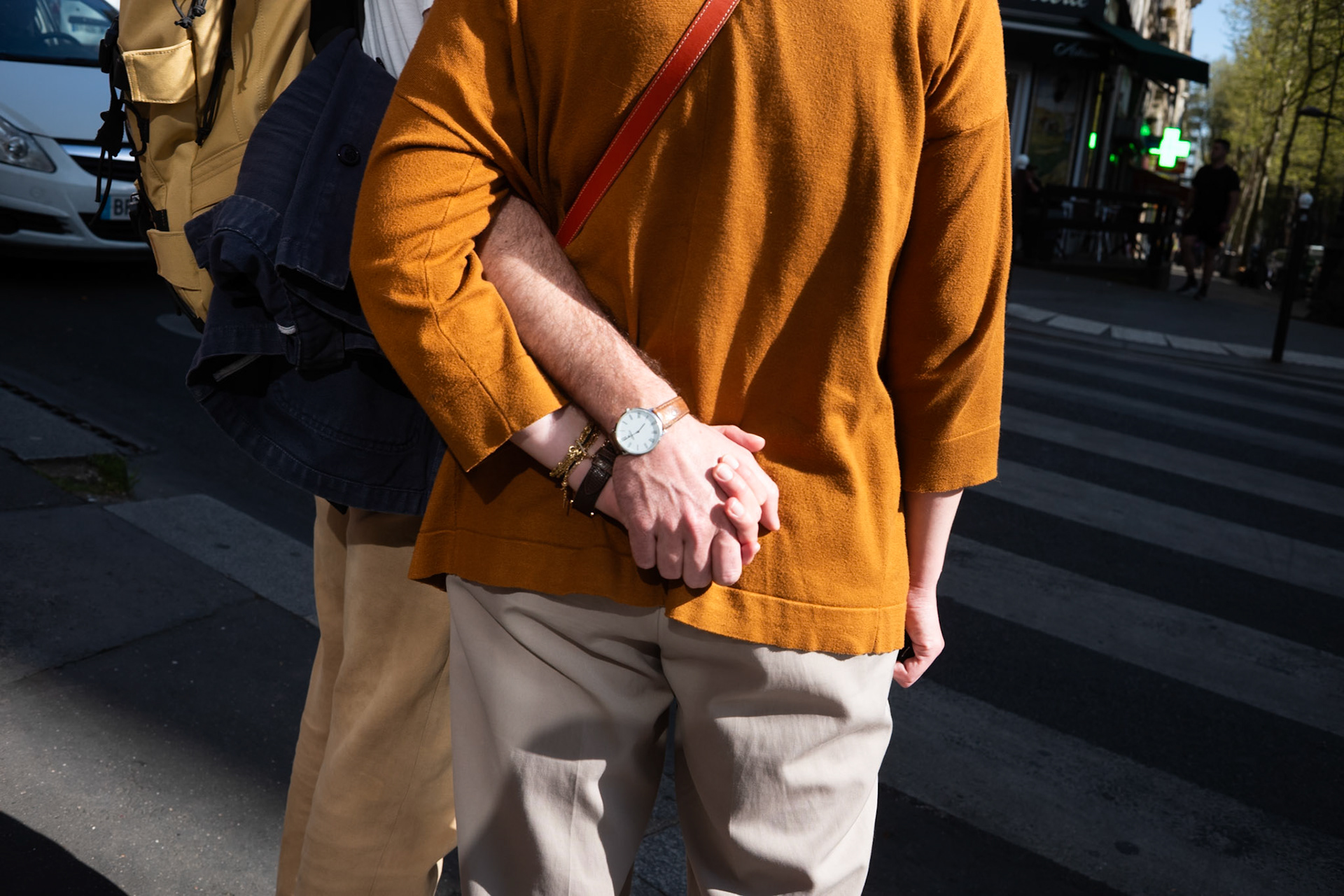 Gros plan sur deux personnes enlacées vues de dos, leurs mains entrelacées reposant derrière le dos de l’une d’elles, avec la lumière rasante soulignant les couleurs chaudes de leurs vêtements.