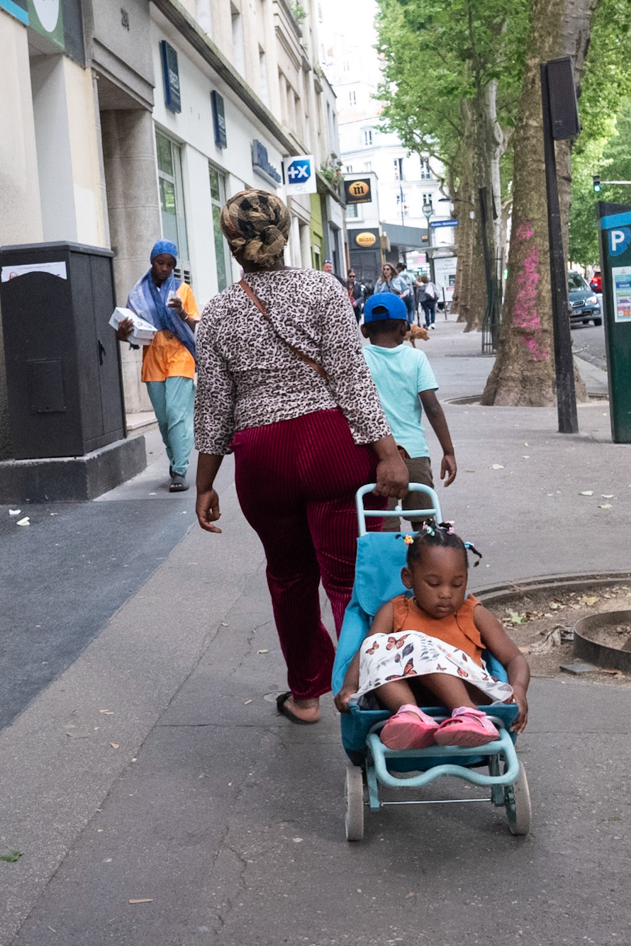 Scène de rue quotidienne : une femme tire une petite fille sur son caddie..
