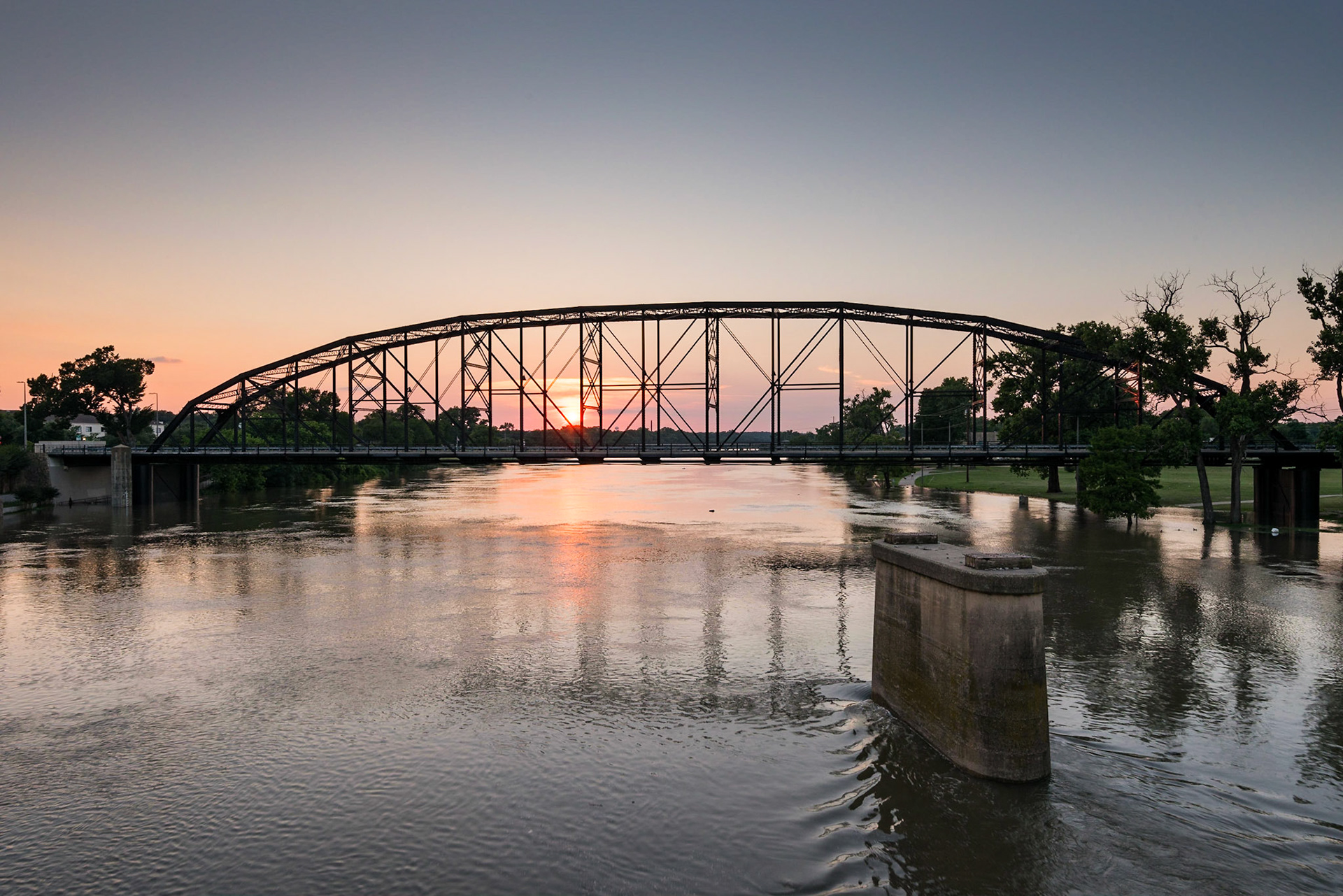I was in Waco for an airshow and decided to go downtown and see the bridges. I photographed sunset through the Washington Avenue Bridge (the Waco Steel Bridge) from the Waco Suspension Bridge. It's an extraordinary example of a through-truss bridge (specifically a Pennsylvania truss), spanning 450 feet over the Brazos River. On this particular day, the Brazos was still at flood stage, as can be seen in the park at right, because of heavy rains in Central Texas the week before.Date: 6 June 2015Location: Waco, Texas, United StatesOriginal resolution: 36 MPProcessing: Processed from RAW using Adobe Photoshop Lightroom 6