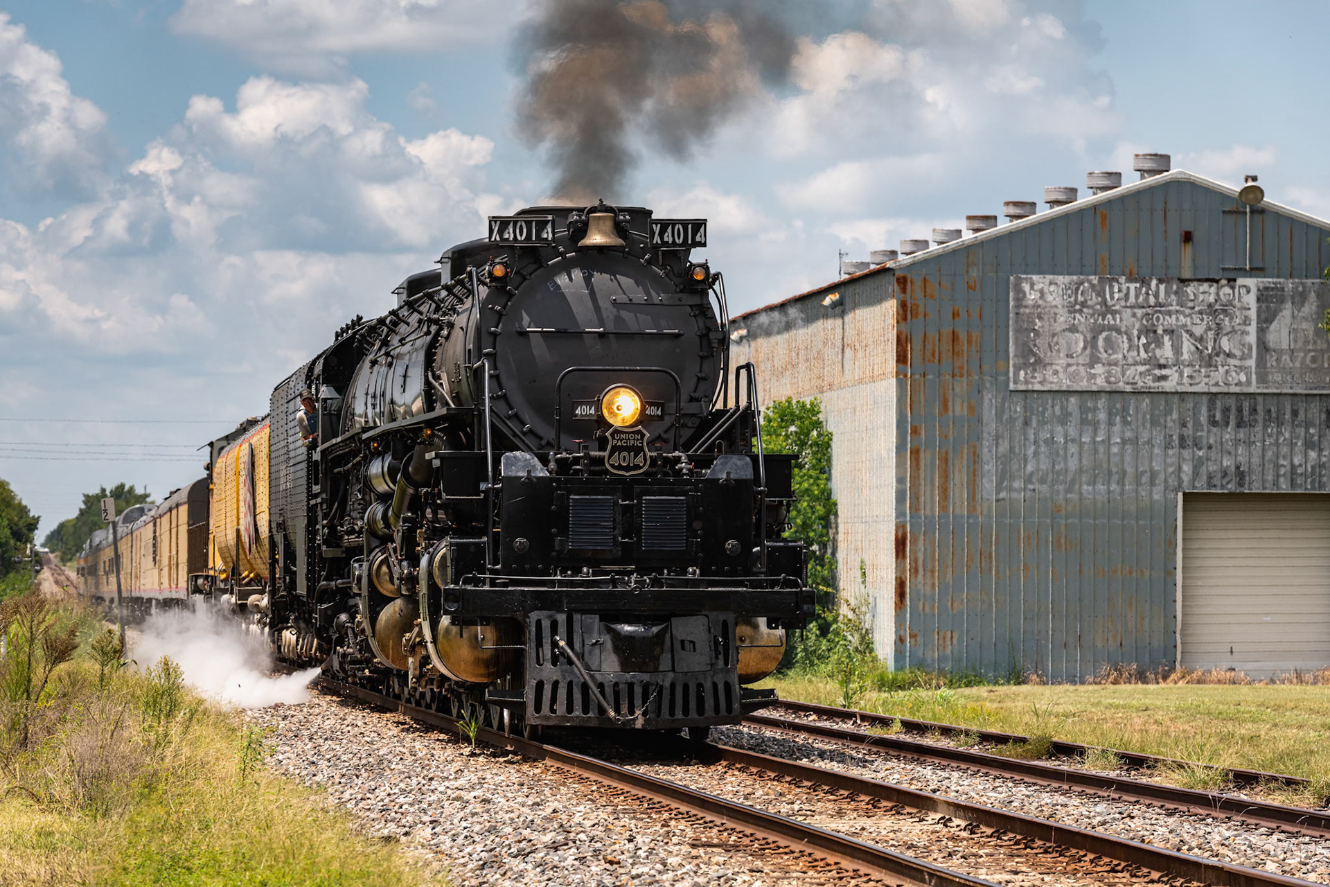 I tried to chase and get ahead of Union Pacific 4014 from College Station to Waller. I walked up and down a couple of blocks in Waller until I finally settled on this position, diagonal to a warehouse. The warehouse offered the advantage of blocking out traffic on the highway on the opposite side. It also provides some interesting texture to the photo.One other interesting opportunity provided by the warehouse is that it makes the photo a bit timeless. Unless you know a lot of specifics about thie composition of this train (like when the water tenders were built), you can't really determine in which time period this photo was taken (of course, being a digital photo does narrow it down).UP 4014 is the only operating model of the twenty-five Big Boy 4-8-8-4 single-expansion steam locomotives built by American Locomotive Company (ALCO) for hauling freight through the Wasatch Range. At about 132 feet in length with its tender and 600 tons of weight, its the largest steam locomotive ever built.Date: 16 August 2021Location: Waller, Texas, United StatesOriginal resolution: 45 MPProcessing: Processed from RAW using Adobe Photoshop Lightroom Classic 10