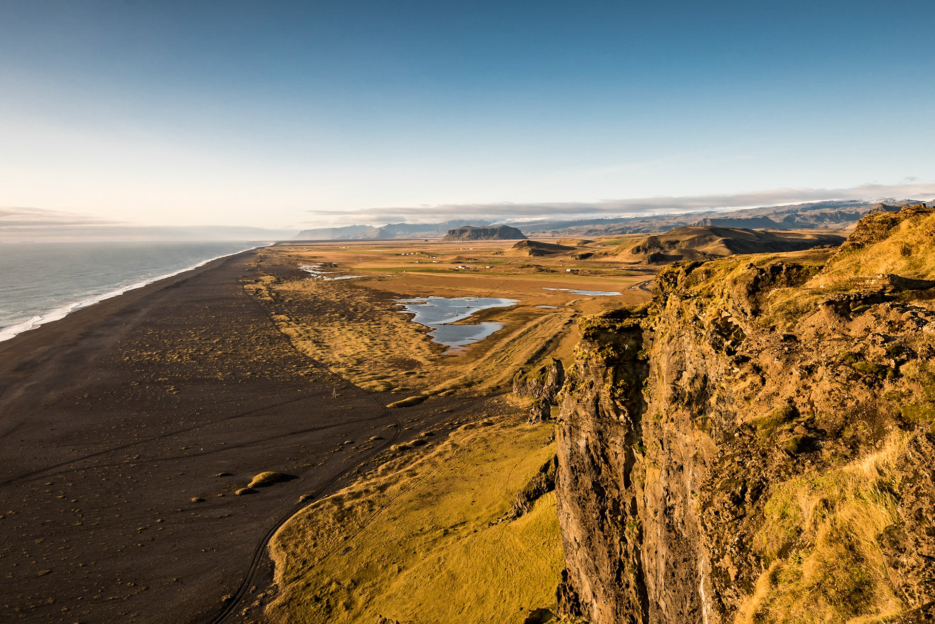 We were on the Dyrhólaey promontory when I took this photo. The rock bluff on the right anchors the foreground, while the black sand beach runs out to the horizon.Date: 16 October 2017Location: Vik, IcelandOriginal resolution: 36 MPProcessing: Processed from RAW using Adobe Photoshop Lightroom Classic CC 8