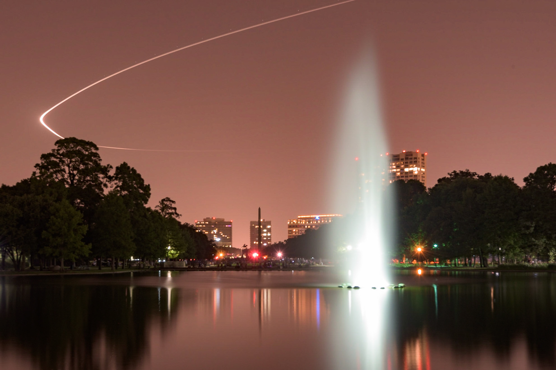 We were waiting on the Independence Day fireworks to start at Hermann Park, when I noticed the planes flying into Hobby airport were making their approach over the park. I decided to see what kind of light trail they would make. In this case, a Southwest 737 carved out a beautiful arc of light that allowed me to capture the fountain in the foreground.Date: 4 July 2015Location: Houston, Texas, United StatesOriginal resolution: 36 MPProcessing: Processed from RAW using Adobe Photoshop Lightroom 6