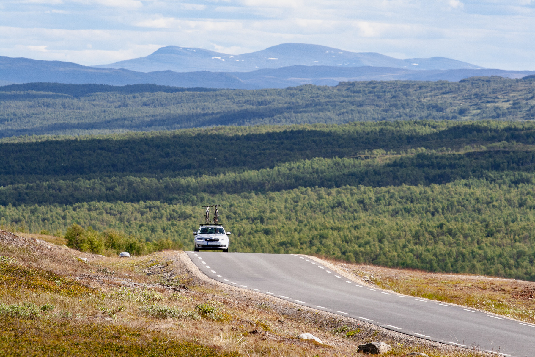 A silver metallic car on the Stuggadalsvegen/Tydalsvegen, with mountains in the background