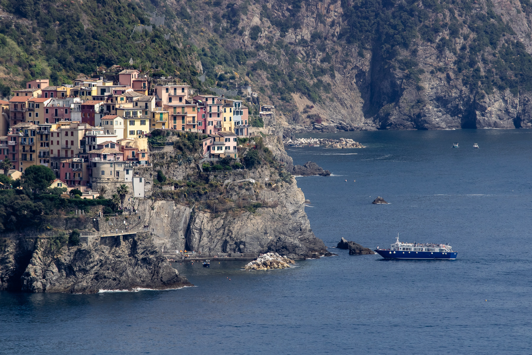 Long-distance view at Manarola from Corniglia. A tourboat is approaching the tiny harbour.