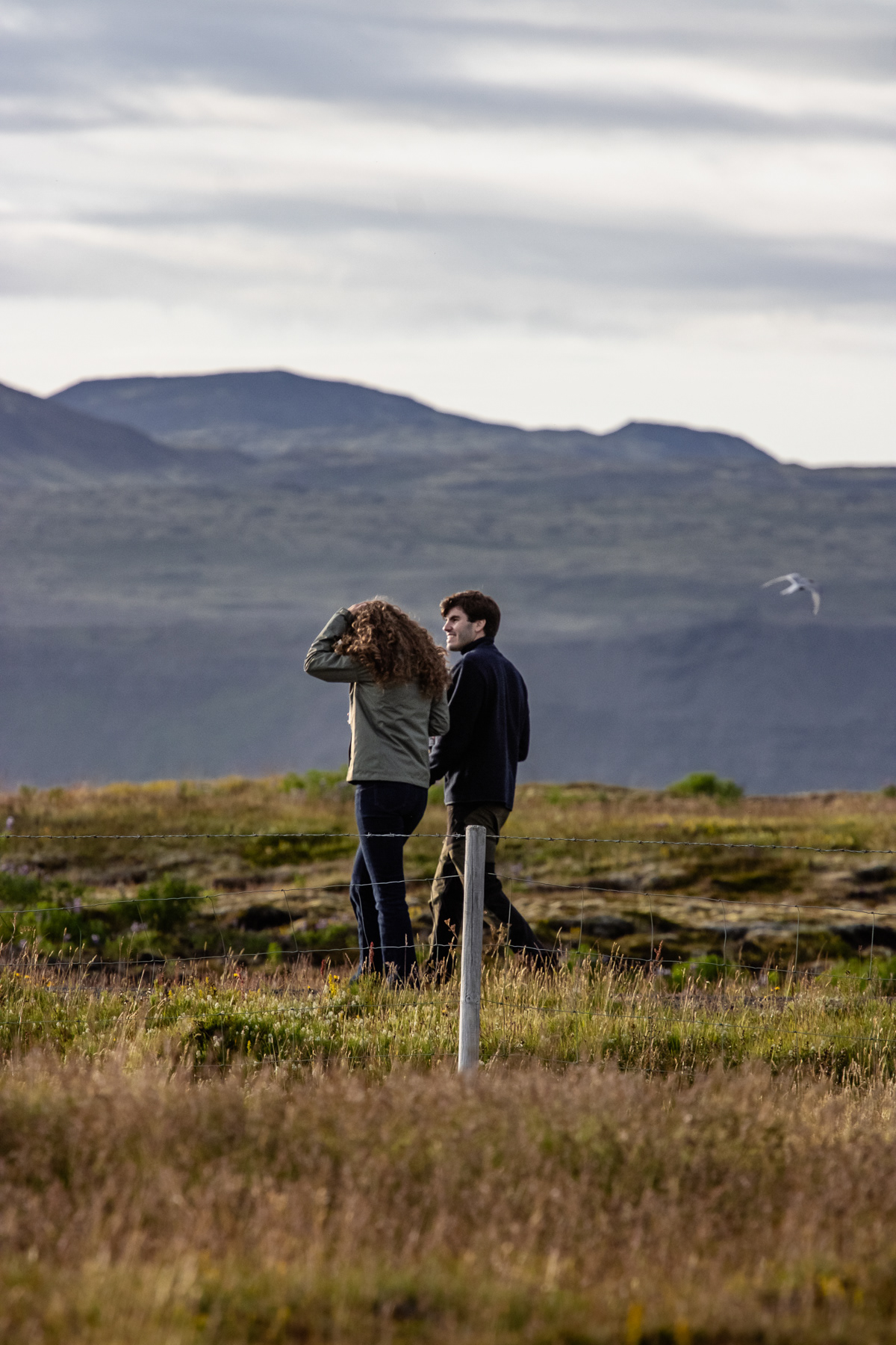A young couple taking a walk through coastal grassy plains, Southwestern A weathered beach home in Southwestern Suðurland. 