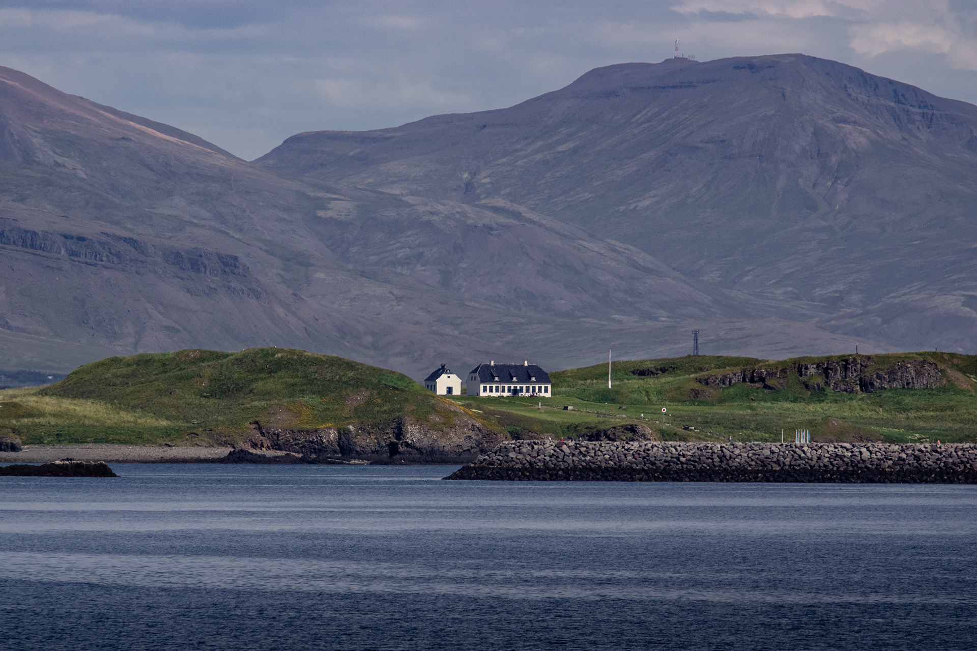 The island of Viðey with the Viðey House restaurant against the background of the Reykjavíkurborg mountains.