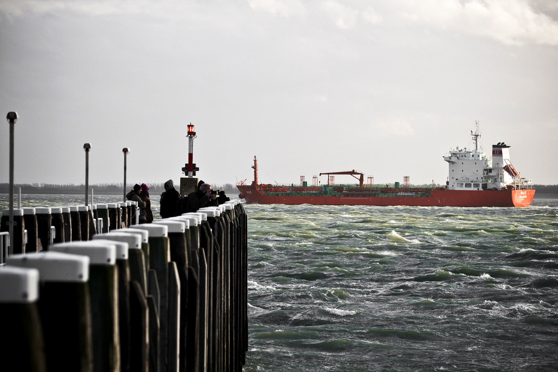 A pier and a red vessel passing