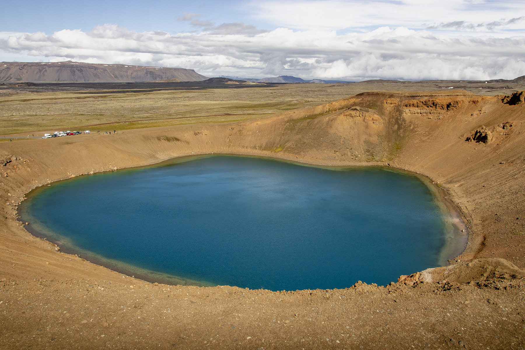 The blue-water Krafla crater lake, with parking lot for perspective, against the backdrop of the vast Leirhnjúkur crater.