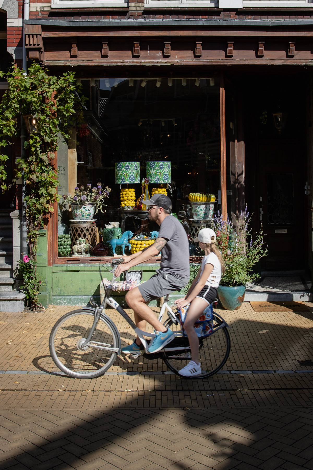 Cyclist and passenger in a centre street, passing a shop.