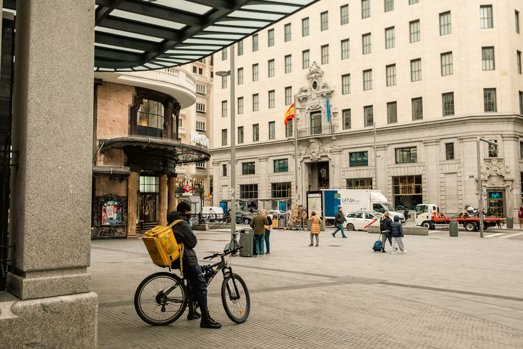 A bicycle food courier waits underneath the canopy of the Gran Via metro station.